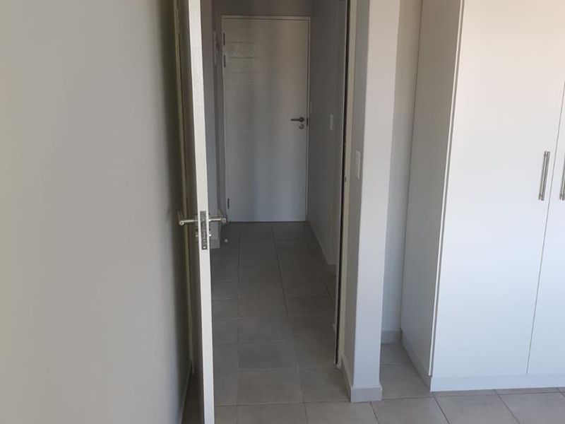 A clean, neutral-toned hallway featuring tiled flooring and a built-in wardrobe, leading to an adjacent room.