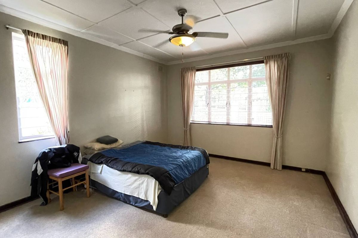 A spacious bedroom featuring a ceiling fan, carpeted flooring, and large windows that provide ample natural light.