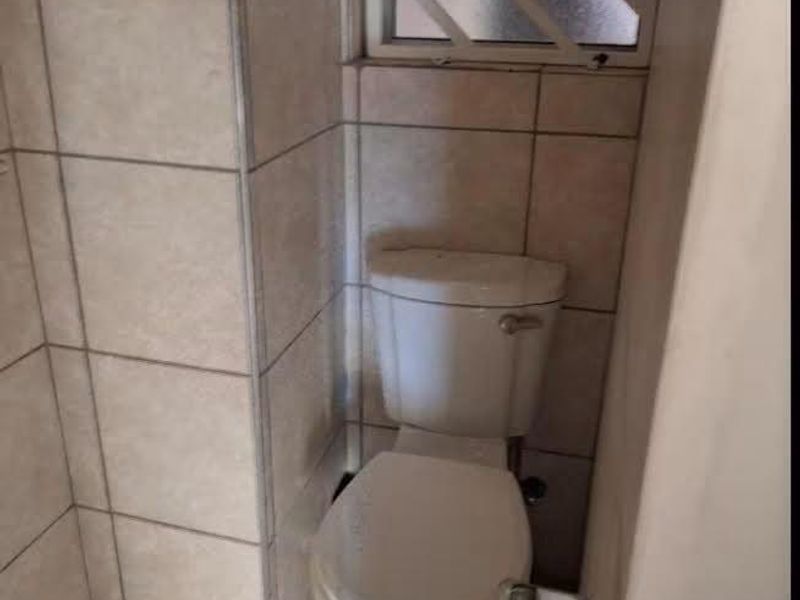 A compact bathroom featuring tiled walls and flooring, equipped with a standard toilet and a window fitted with security bars.