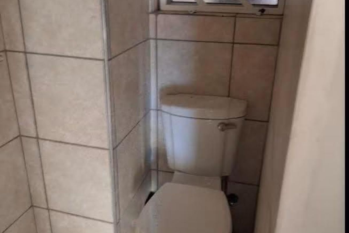 A compact bathroom featuring tiled walls and flooring, equipped with a standard toilet and a window fitted with security bars.