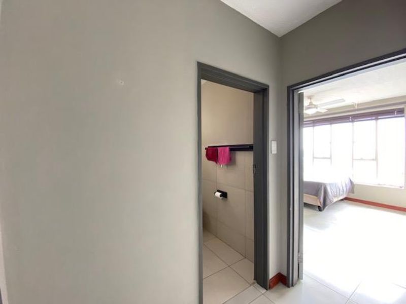 A neutral-toned hallway providing access to a bathroom and a bedroom with large windows.