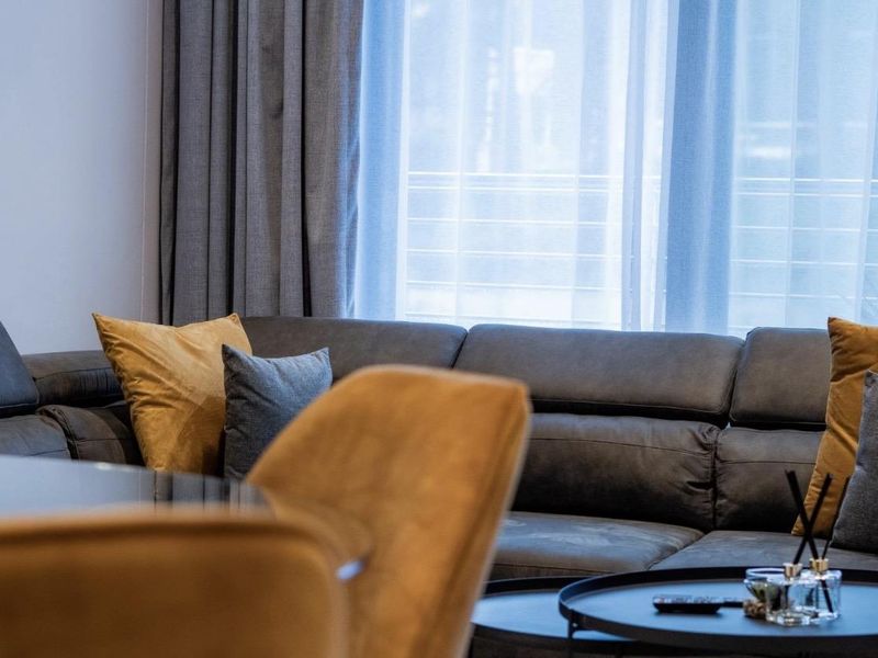 A comfortable living room area featuring layered window treatments with sheer curtains and heavy drapes, providing natural light control and privacy.