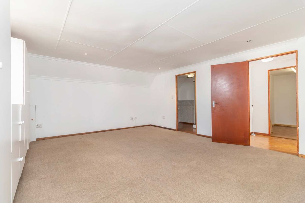 A spacious, empty bedroom featuring neutral carpeting, built-in cupboards, and direct access to an adjoining bathroom and hallway.