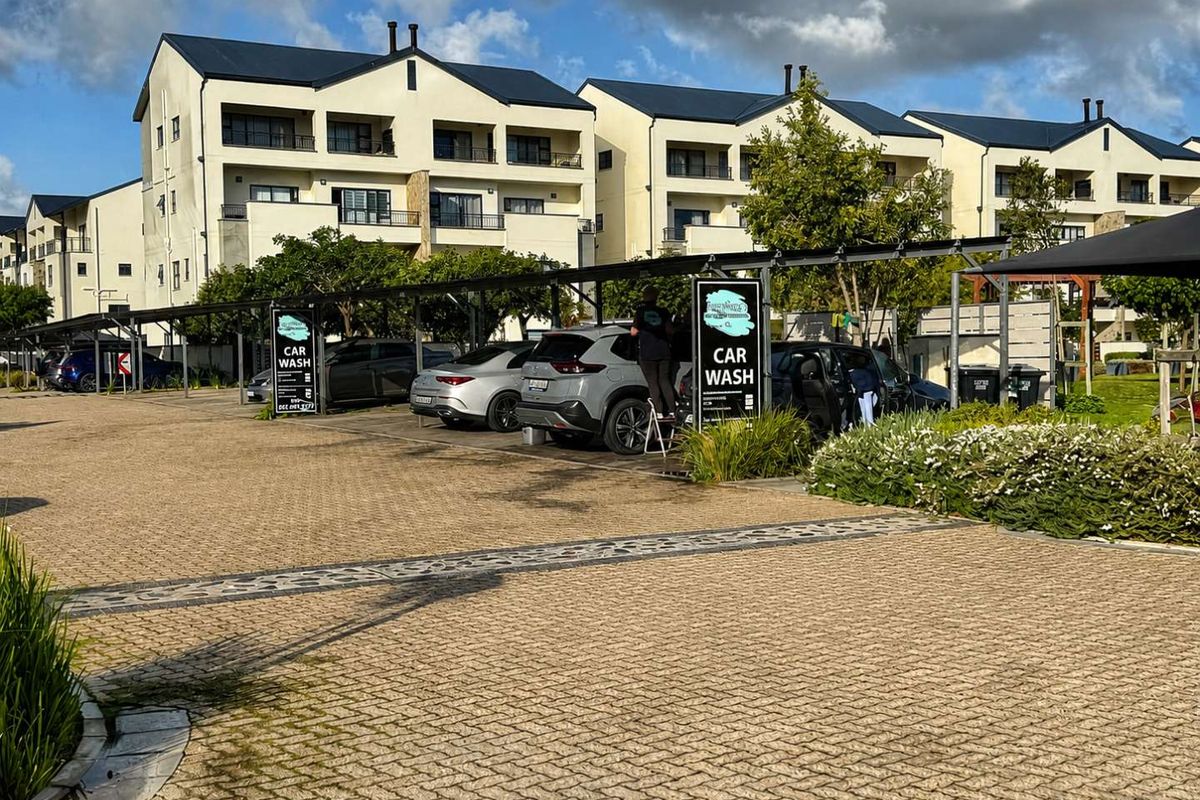 Exterior view of the apartment complex featuring paved parking areas with covered bays and well-maintained landscaped garden surroundings.