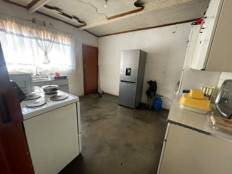 A dated kitchen featuring basic cabinetry, a sink, and an electric stove, requiring significant renovation and cosmetic updates to improve its condition.