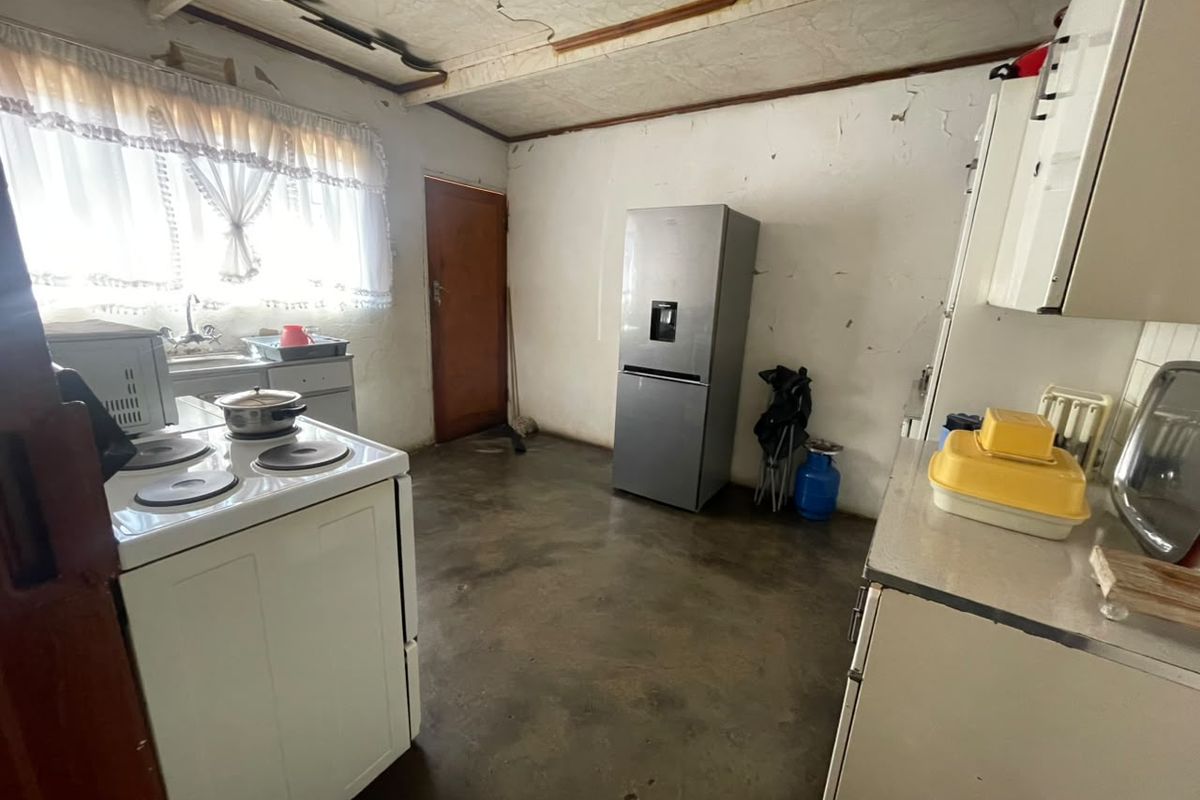 A dated kitchen featuring basic cabinetry, a sink, and an electric stove, requiring significant renovation and cosmetic updates to improve its condition.