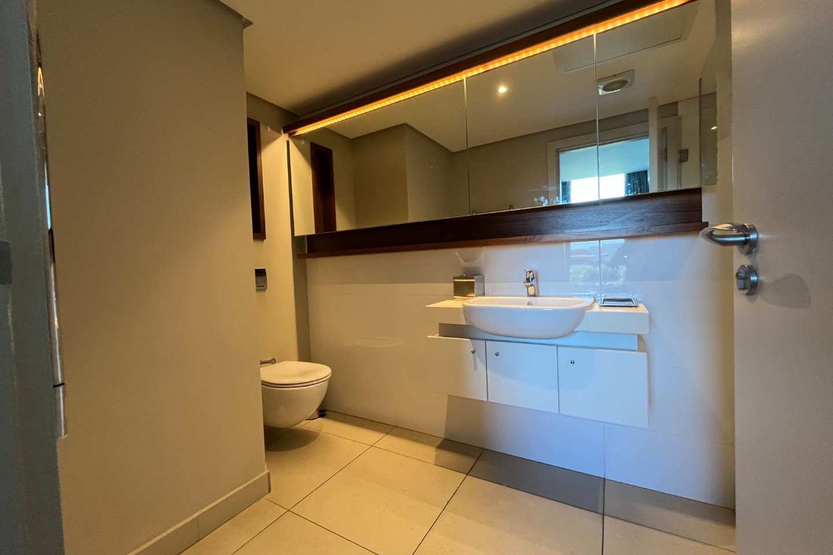 Modern bathroom featuring a wall-mounted vanity with integrated basin, large mirror with ambient lighting, and a wall-hung toilet.