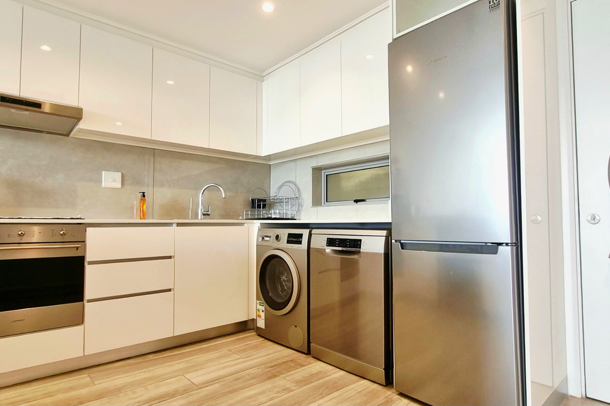 Modern kitchen featuring sleek white cabinetry, stainless steel appliances, integrated oven, extractor fan, and wood-look flooring.