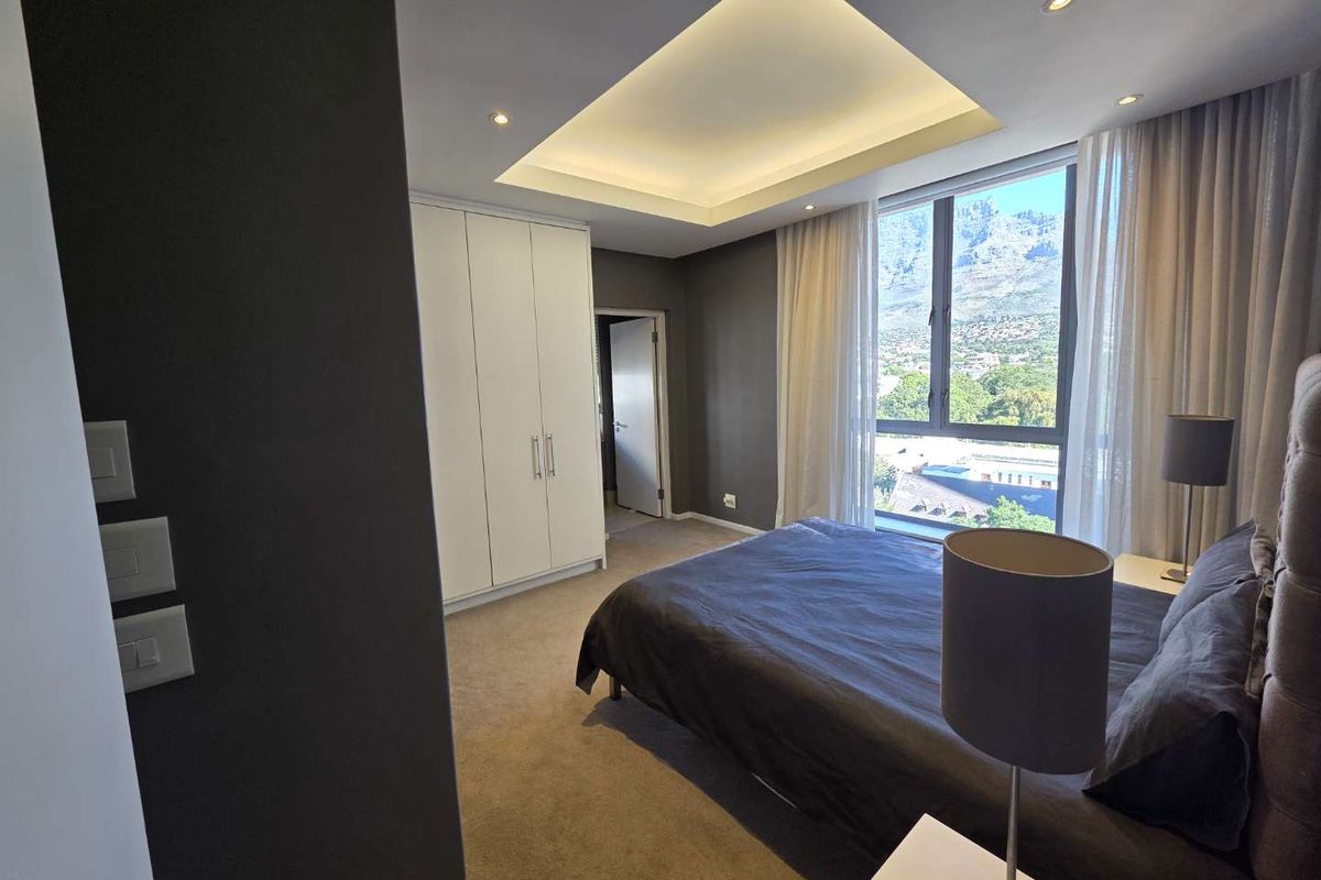 A modern bedroom featuring built-in cupboards, a recessed ceiling with ambient lighting, and a large window offering scenic mountain views.