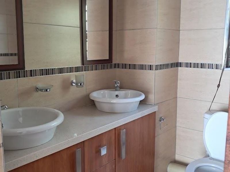 A clean, modern bathroom featuring a double vanity with vessel sinks, stone countertop, built-in wooden cabinetry, and neutral wall tiling.
