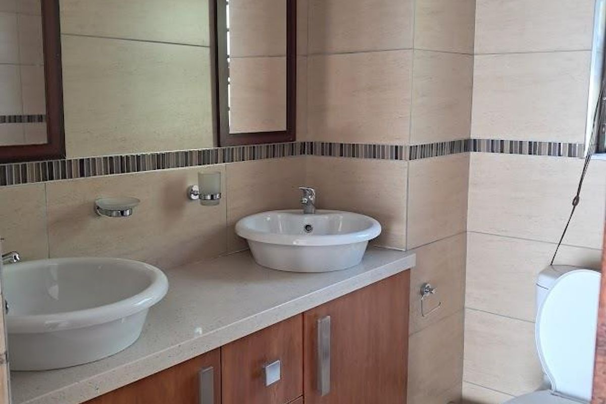 A clean, modern bathroom featuring a double vanity with vessel sinks, stone countertop, built-in wooden cabinetry, and neutral wall tiling.