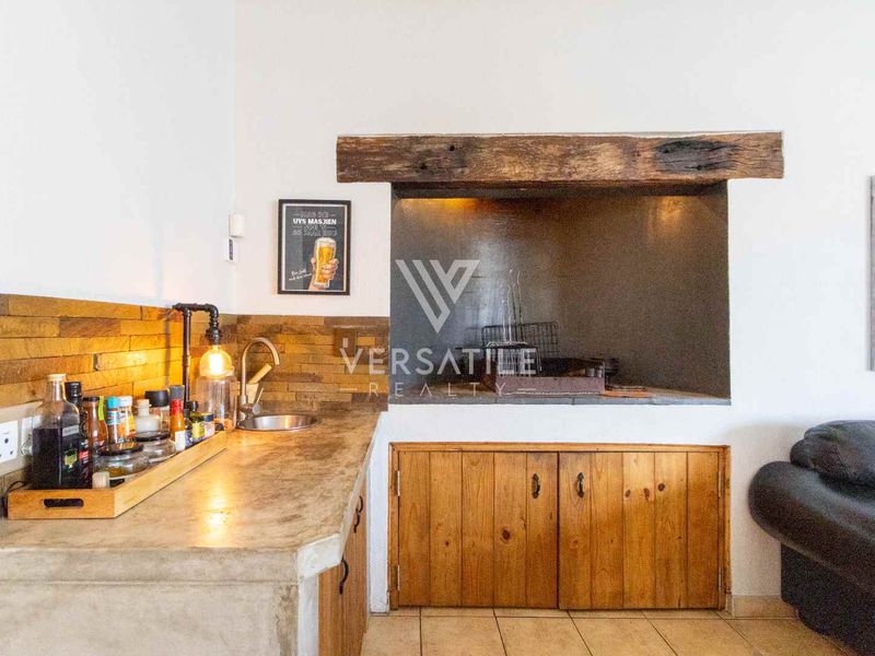 Indoor entertainment area featuring a built-in braai with a rustic timber mantel, concrete countertop, and integrated sink with wooden cabinetry.