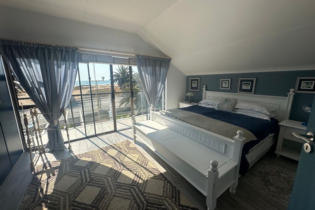 A bright bedroom featuring vaulted ceilings, tiled flooring, and large sliding glass doors that open onto a balcony with scenic coastal views.