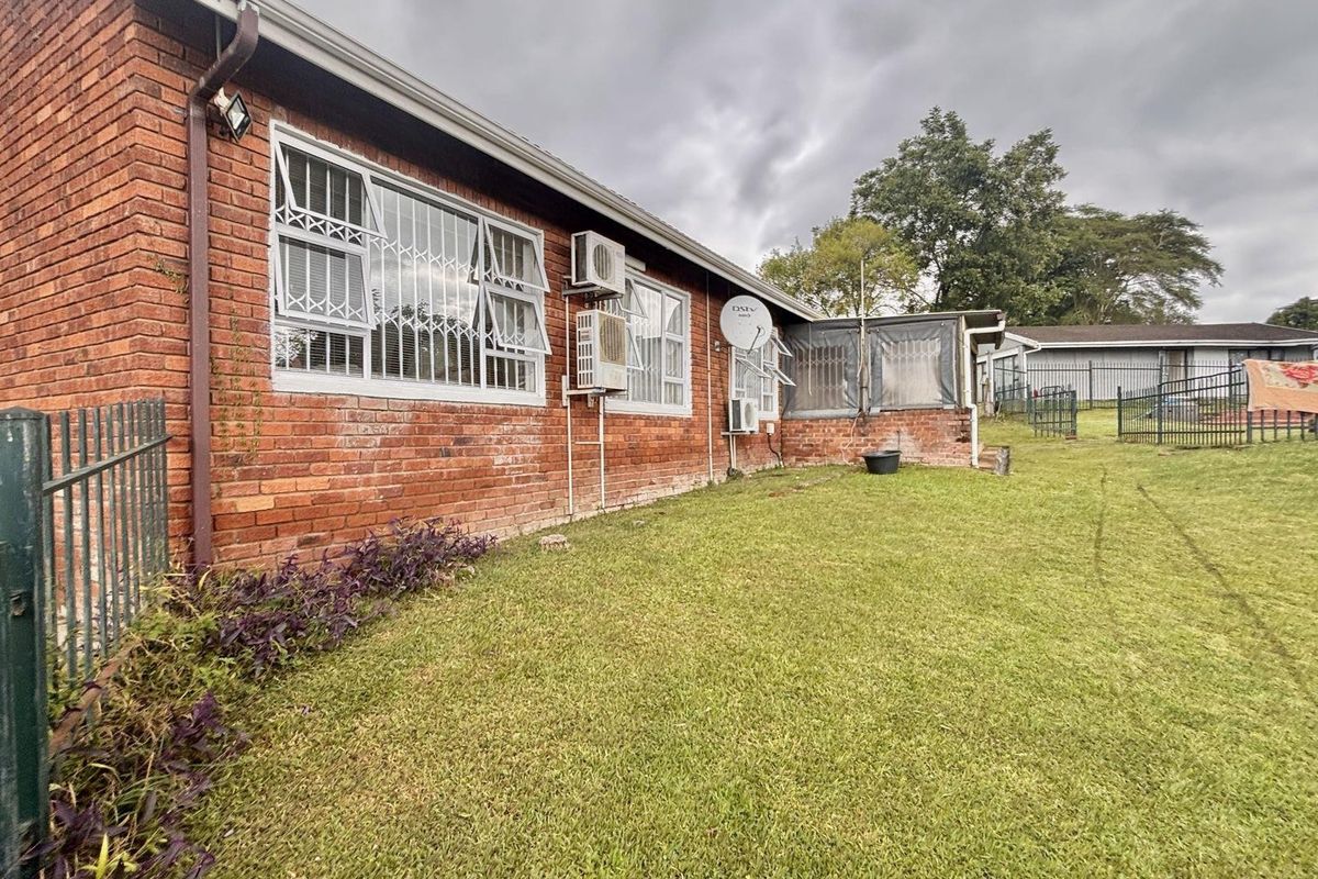 Rear view of the property featuring a brick facade, security-barred windows, wall-mounted air conditioning units, and a spacious grass lawn.