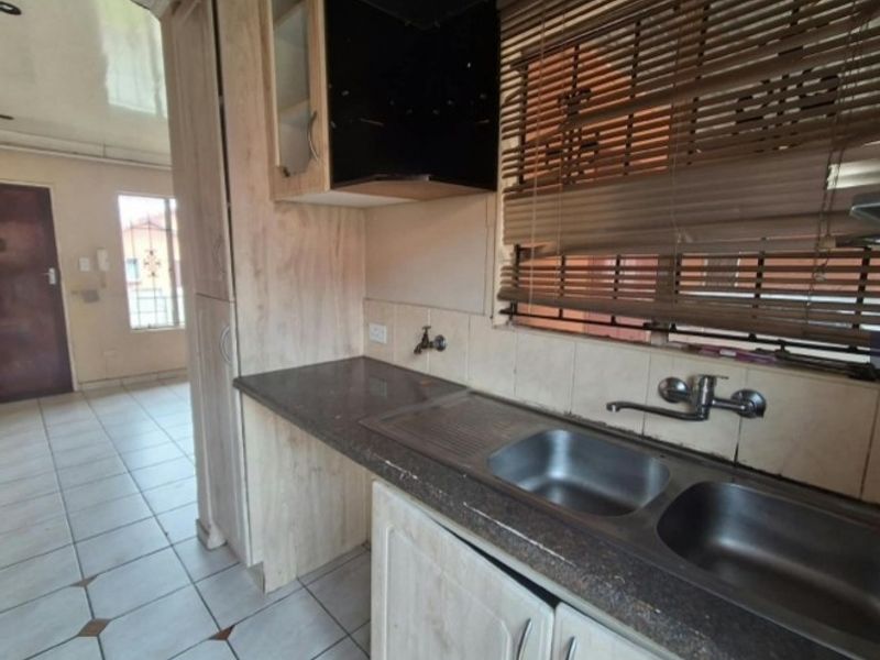 A functional kitchen featuring laminate cabinetry, stone countertops, a double bowl stainless steel sink, and tiled flooring, offering a clean and practical workspace.