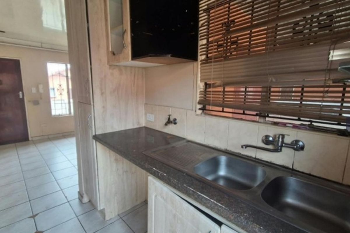 A functional kitchen featuring laminate cabinetry, stone countertops, a double bowl stainless steel sink, and tiled flooring, offering a clean and practical workspace.