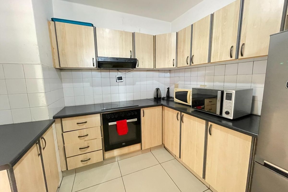 Functional kitchen featuring light wood-finish cabinetry, black countertops, ceramic tile backsplash, and integrated oven with hob, offering a practical layout for daily cooking.