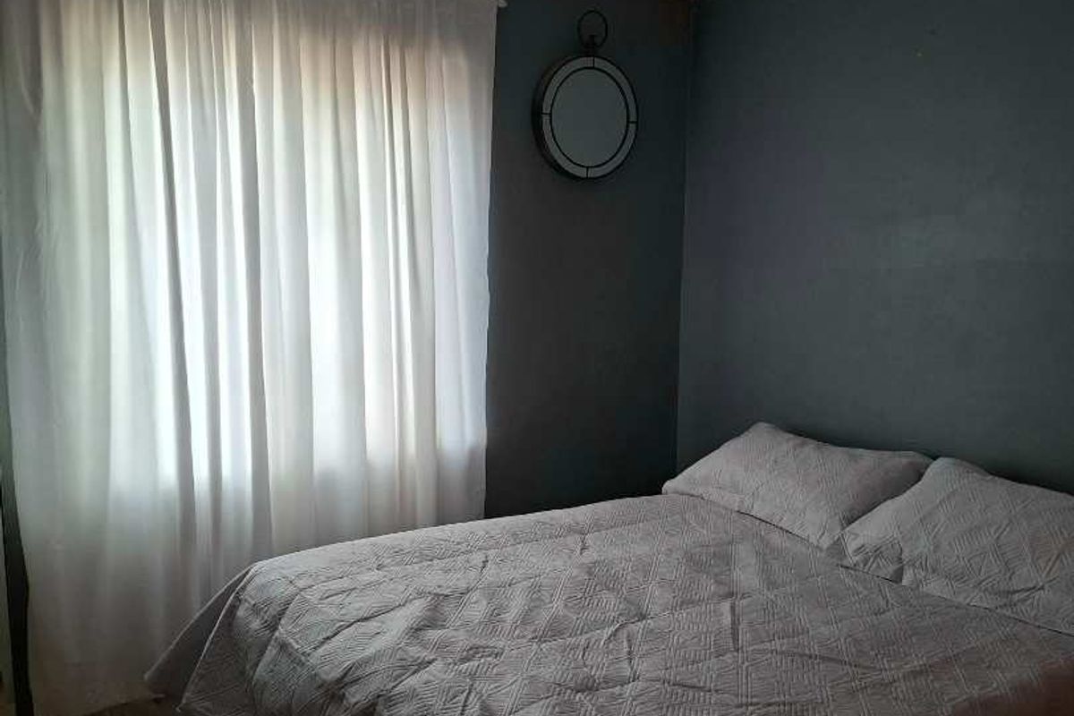A simple bedroom featuring dark-toned walls, a central ceiling light fixture, and a window with curtains.
