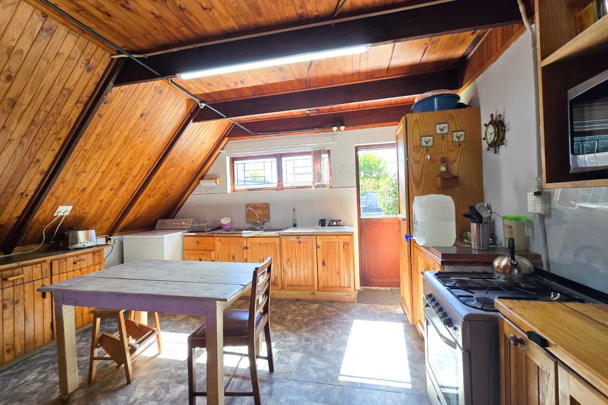 A rustic kitchen featuring timber cabinetry, exposed wooden beams, a gas stove, and vinyl flooring, offering a warm and functional cooking space.