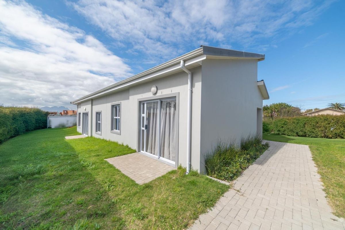 Exterior view of the apartment building featuring a paved walkway, sliding glass doors, and surrounding lawn area.