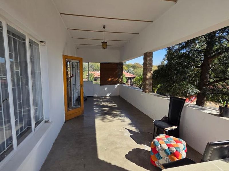 A covered outdoor balcony featuring concrete flooring, a stone-clad pillar, and a security gate, offering a spacious area for outdoor relaxation.