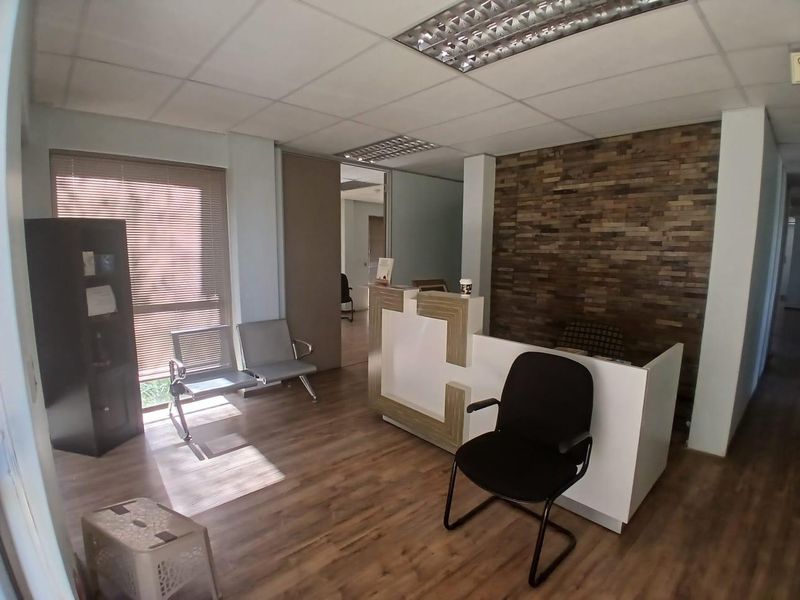Professional office reception area featuring a modern reception desk, stone veneer accent wall, laminate flooring, and recessed ceiling lighting.