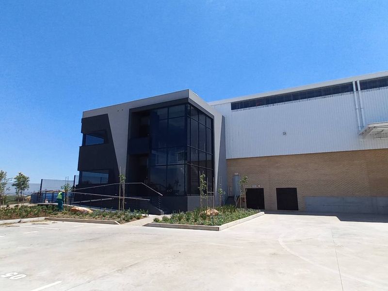 Modern industrial facility featuring a glass-fronted office section, metal cladding, and a large roller shutter door with an expansive concrete yard area.