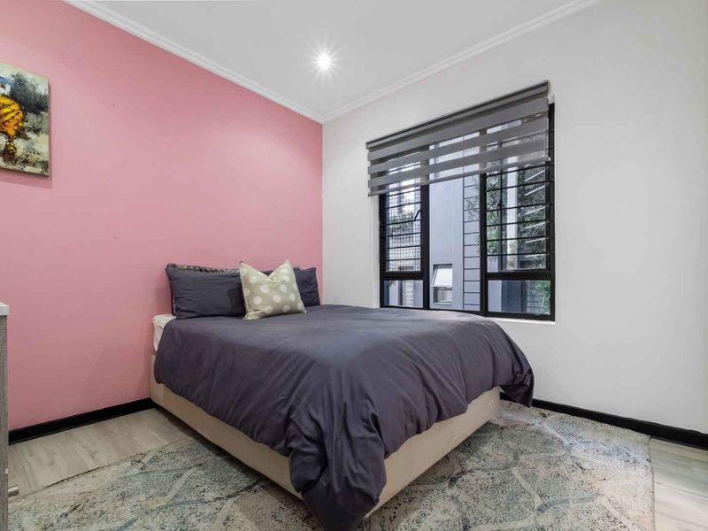 A well-maintained bedroom featuring laminate flooring, a built-in wardrobe, and a modern roller blind, finished with a feature wall.
