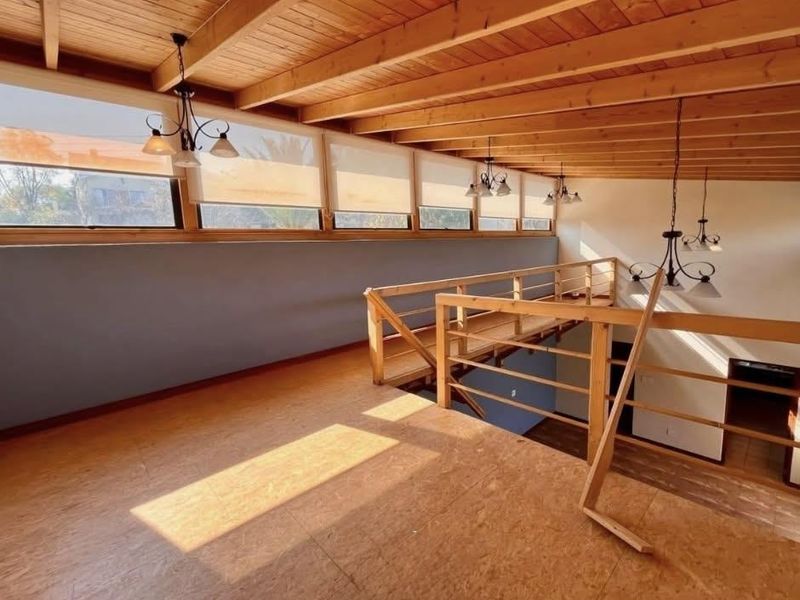 Spacious mezzanine living area featuring exposed timber beam ceilings, warm timber flooring, and large clerestory windows providing abundant natural light.