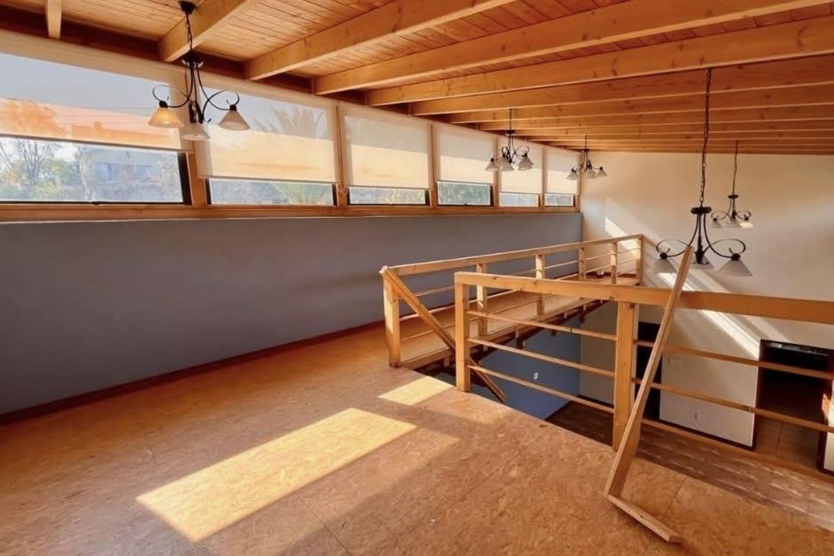 Spacious mezzanine living area featuring exposed timber beam ceilings, warm timber flooring, and large clerestory windows providing abundant natural light.