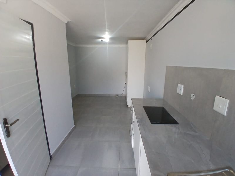 A modern, minimalist kitchen area featuring sleek cabinetry, a stone-look countertop with an integrated hob, and neutral tiled flooring in an open-plan layout.