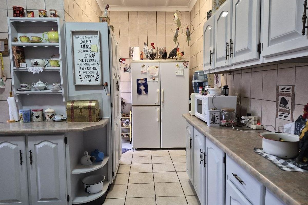 A functional kitchen featuring white built-in cabinetry, laminate countertops, and full-height ceramic wall tiling with neutral floor tiles.