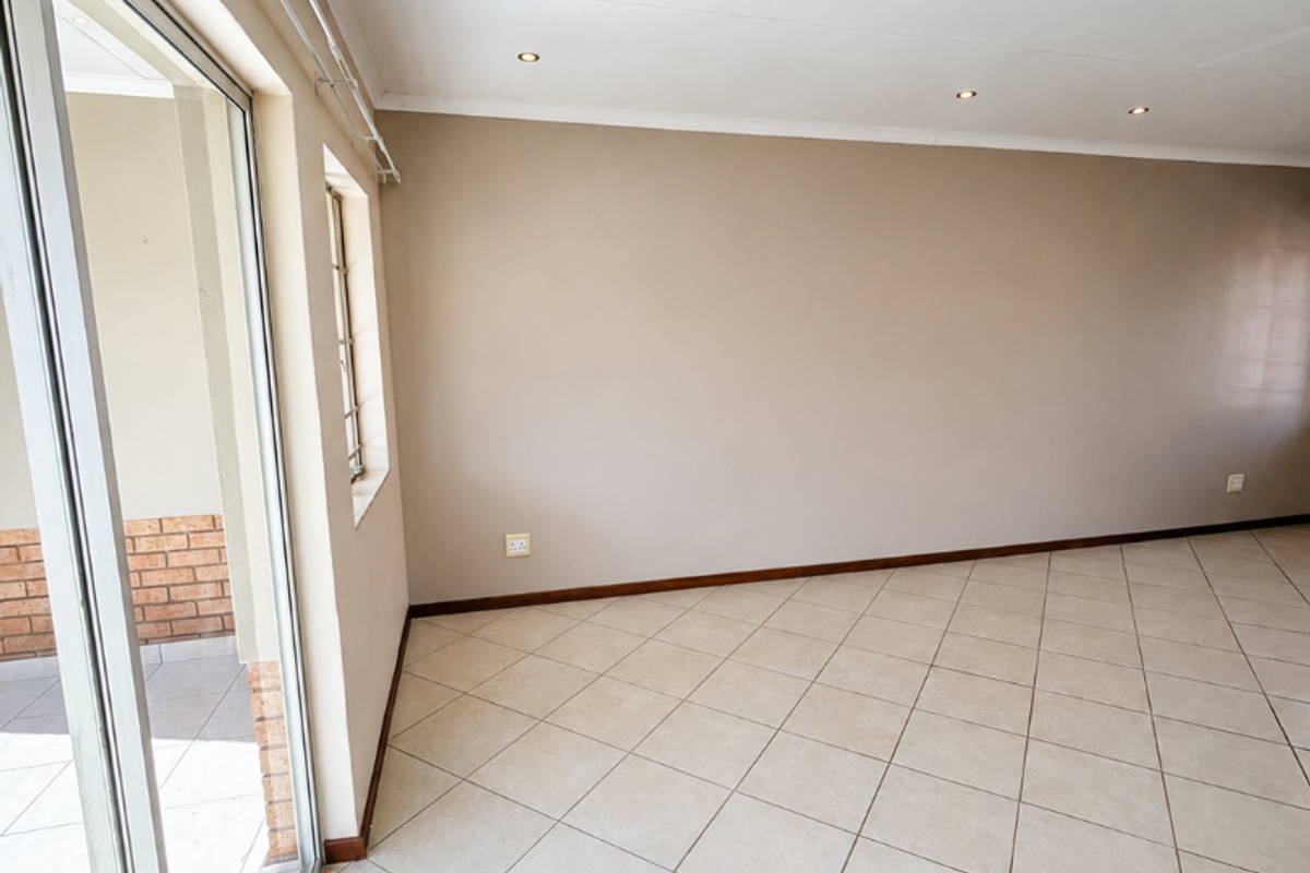 A bright, empty living area featuring neutral tiled flooring, recessed lighting, and a large sliding glass door providing access to the outdoor patio.
