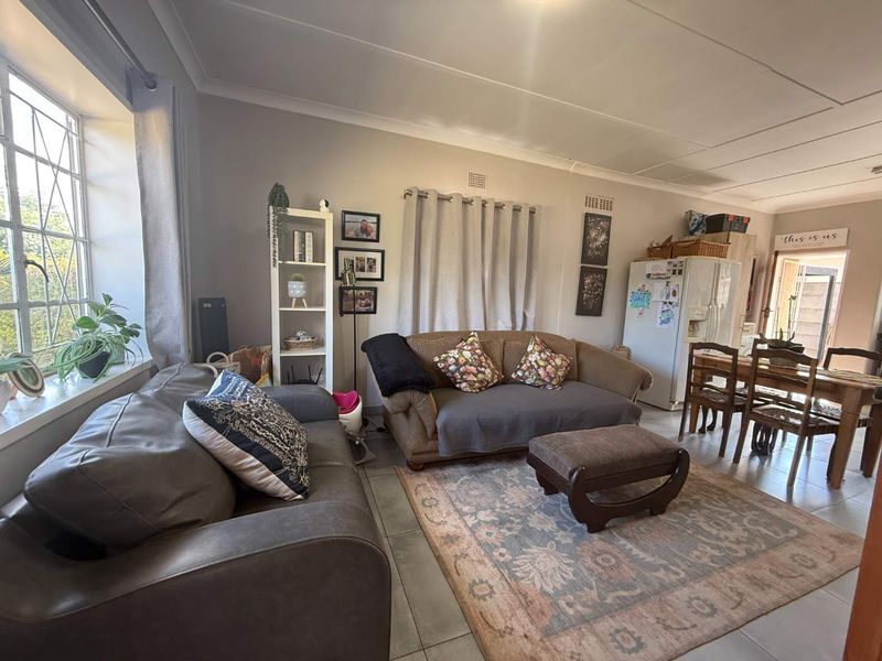 An open-plan living and dining area featuring tiled flooring, coved ceilings, and a large leaded glass window providing natural light.