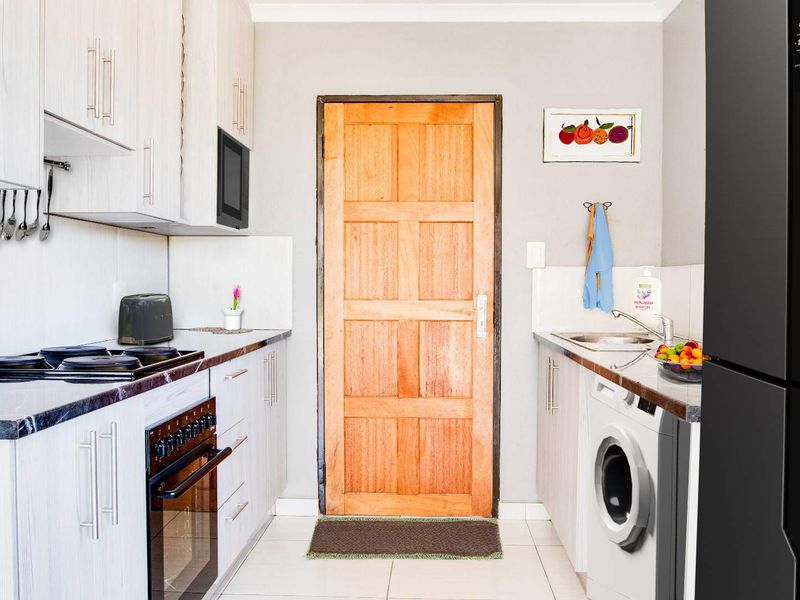 A functional kitchen featuring light-toned cabinetry, dark countertops, built-in oven and stove, and integrated laundry plumbing, finished with tiled flooring.