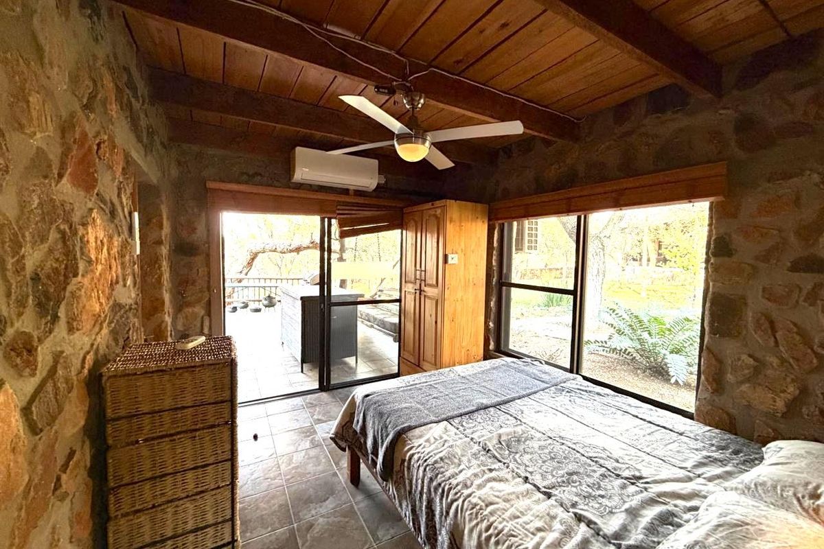 Rustic bedroom featuring exposed timber beam ceilings, stone masonry walls, tiled flooring, and direct access to an outdoor patio area.