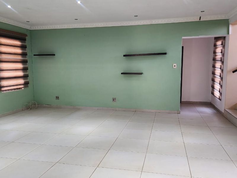A spacious, empty living area featuring neutral tiled flooring, recessed downlighting, decorative ceiling cornices, and modern zebra blinds on the windows.