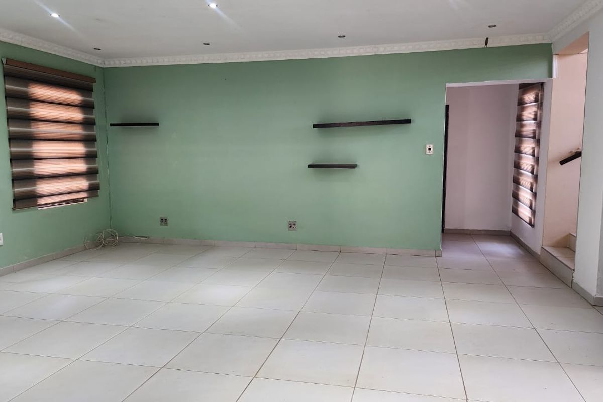 A spacious, empty living area featuring neutral tiled flooring, recessed downlighting, decorative ceiling cornices, and modern zebra blinds on the windows.