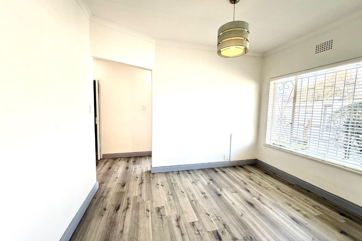 A bright, empty bedroom featuring modern wood-look laminate flooring, neutral walls, and a fitted pendant light fixture.