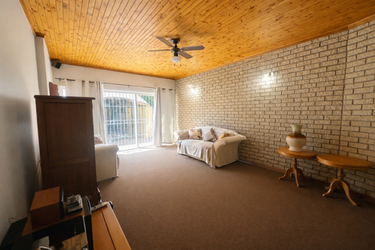 Spacious living room featuring a textured brick feature wall, timber-clad ceiling, ceiling fan, and sliding glass doors providing access to the exterior.
