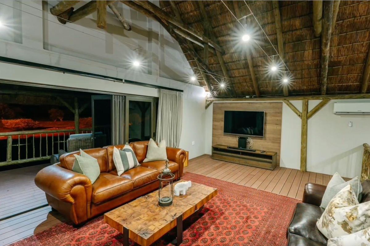 Spacious lodge living area featuring a high vaulted thatched ceiling with exposed timber beams, wooden flooring, and large sliding doors opening to a deck.