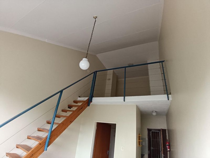 Open plan living area featuring a timber staircase leading to a mezzanine level with metal balustrades and neutral wall finishes.