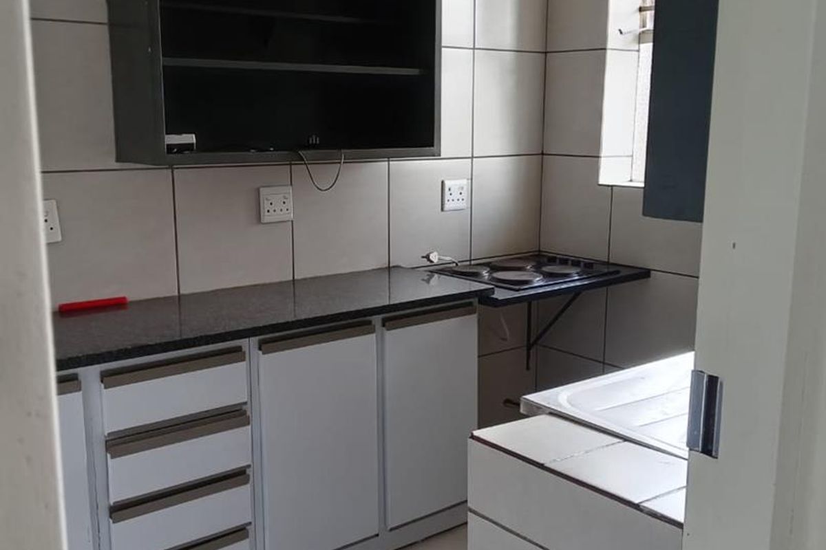 A functional kitchen featuring granite countertops, built-in cabinetry, an electric hob, and tiled finishes throughout.