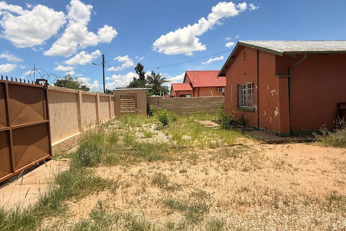 Rear exterior view of the property featuring a perimeter wall, metal gate, and a house with visible exterior paint deterioration.