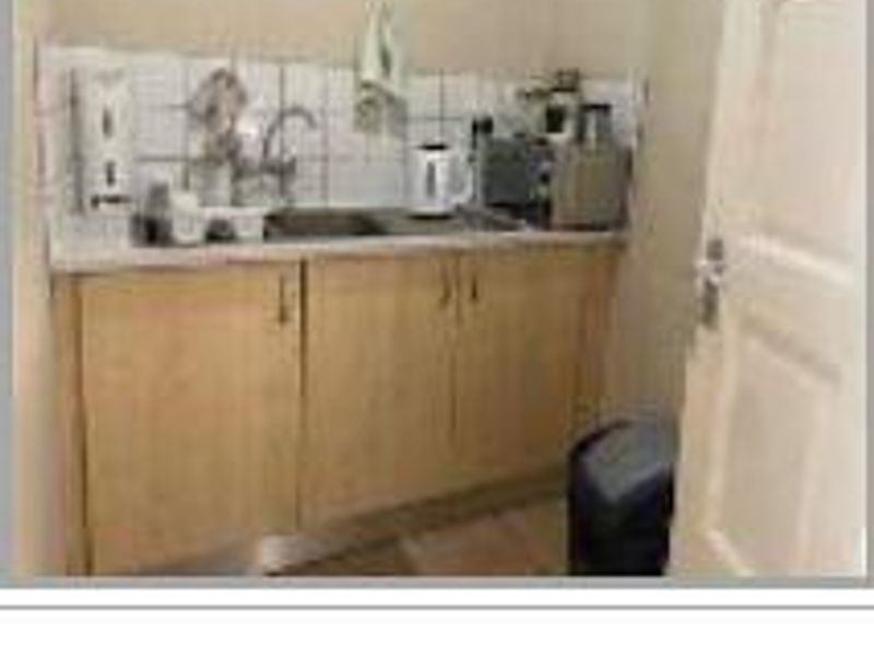 A compact kitchenette area featuring built-in wooden cabinetry, a stainless steel sink, and a tiled backsplash.