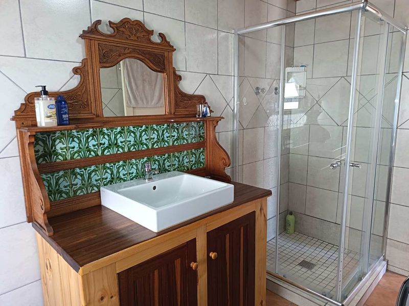 Bathroom featuring a custom wooden vanity with a vessel sink, decorative tiled backsplash, and a glass-enclosed shower with neutral wall tiling.