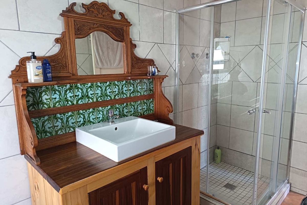 Bathroom featuring a custom wooden vanity with a vessel sink, decorative tiled backsplash, and a glass-enclosed shower with neutral wall tiling.