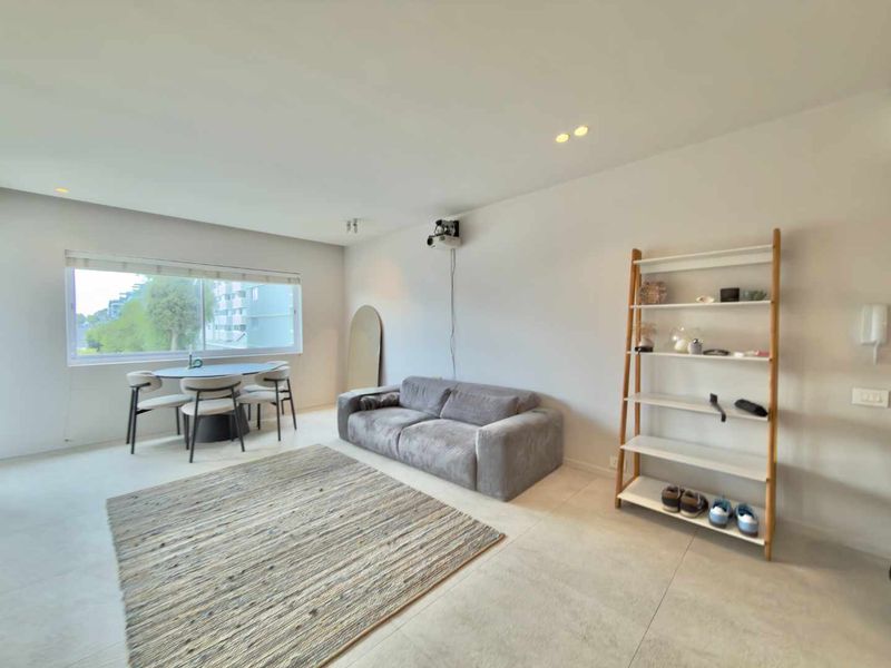 A bright and modern living room featuring tiled flooring, recessed downlighting, and a wall-mounted projector, offering a clean and contemporary living space.