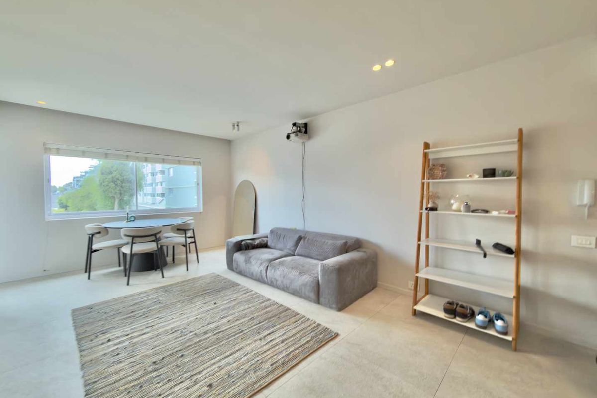 A bright and modern living room featuring tiled flooring, recessed downlighting, and a wall-mounted projector, offering a clean and contemporary living space.