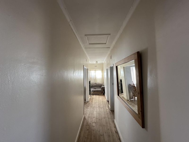 A long, neutral-toned hallway featuring timber flooring and a ceiling access hatch, providing a clean and functional transition space between rooms.
